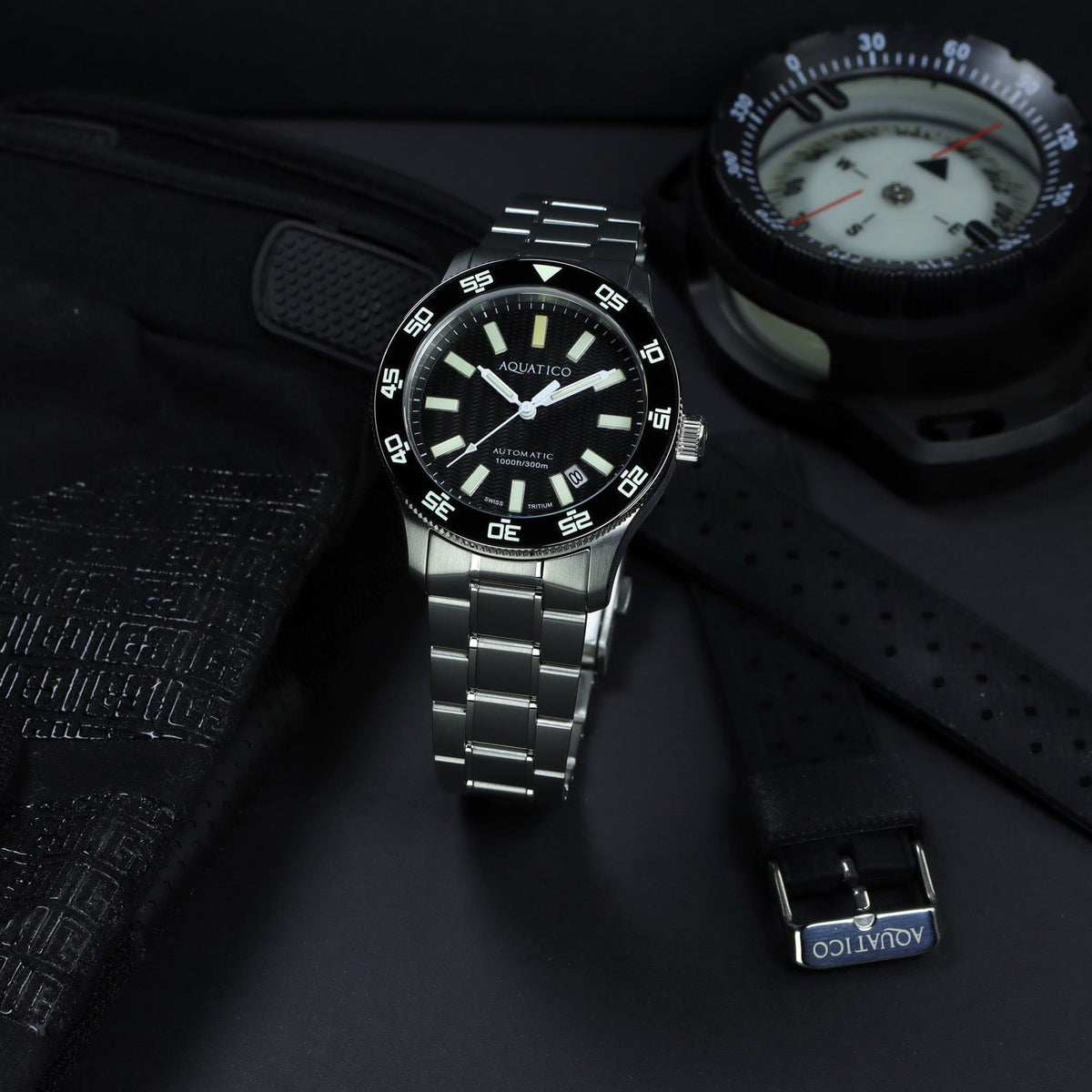 Aquatico Sea Sentinel black dial watch and bracelet beside equipment